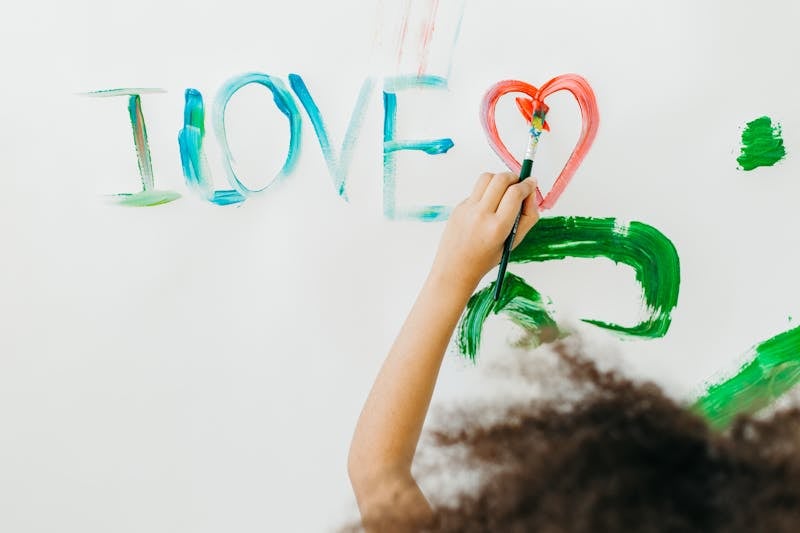 A child paints 'I LOVE' and a heart on a wall, expressing creativity and emotions.