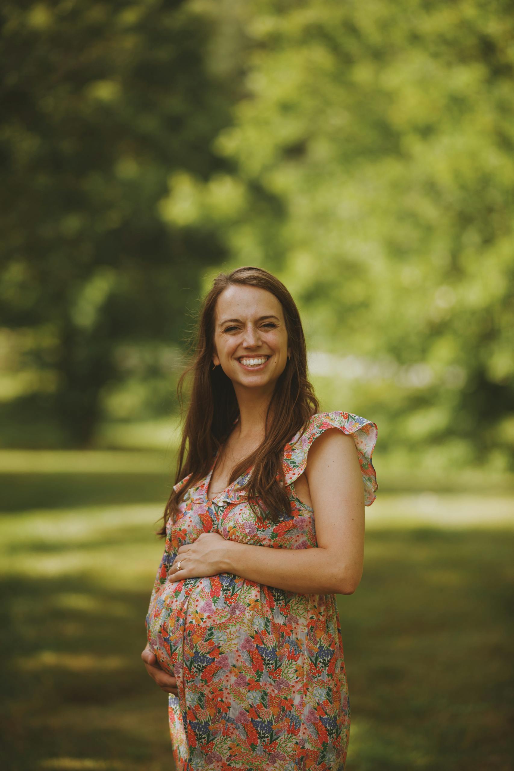 A happy pregnant woman in a floral dress enjoying a sunny day outdoors.